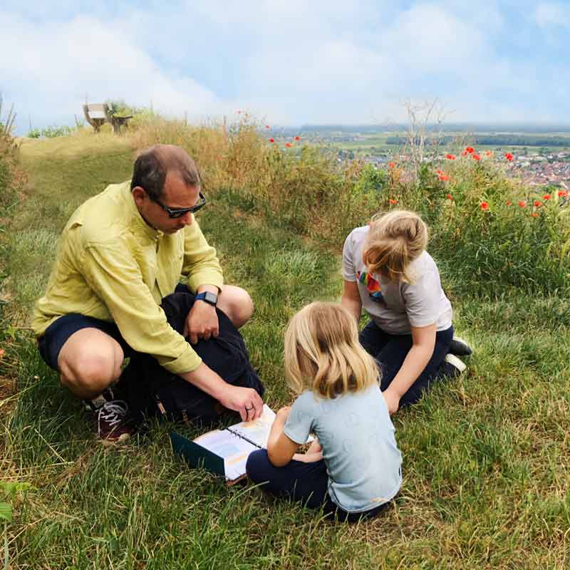 Kinder spielen das Outdoor Escape Abenteuer "Buch der 7 Siegel" in den Weinreben vom Kaiserstuhl mit Ausblick über eine Kleinstadt.