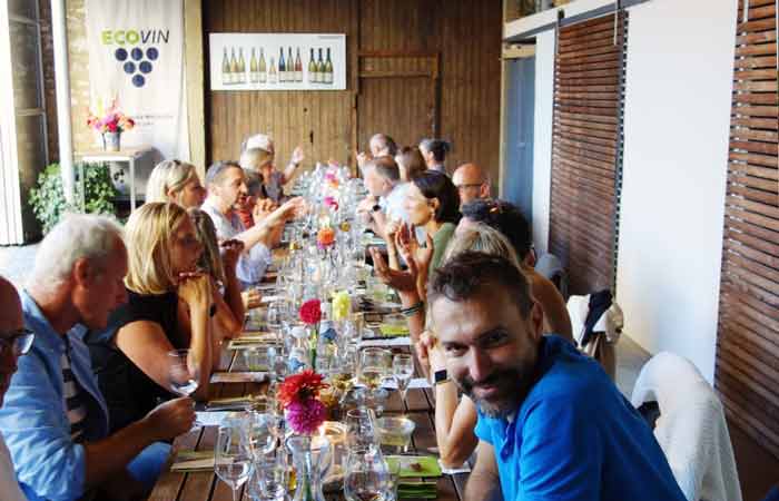 Menschen sitzen an einer langen Tafel bei einer Weinprobe im Innenhof vom Weingut Karl Sonntag in Nittel.