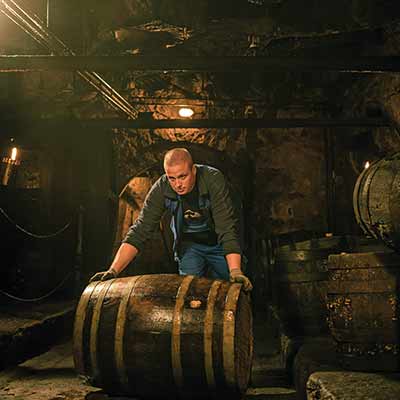 Brauer in traditioneller Kleidung im historischen Kellergewölbe des Brauhaus Faust beim Arbeiten an einem Holzfass.