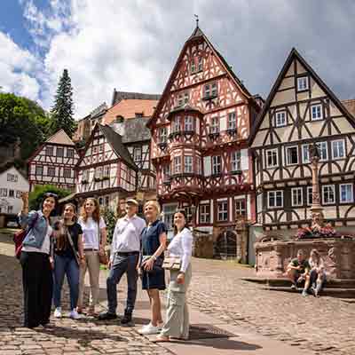 Touristengruppe bei einer Stadtführung auf einem Kopfsteinpflasterweg zwischen historischen Fachwerkhäusern in Miltenberg.
