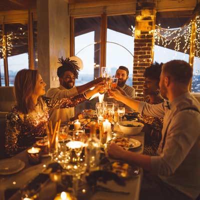 Menschen sitzen an einem weihnachtlich gedeckten Tisch in gemütlicher Atmosphäre und prosten sich zu.