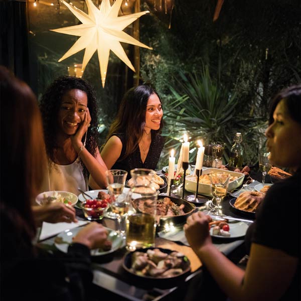 Frauen sitzen an einem weihnachtlich gedeckten Tisch in gemütlicher Atmosphäre und genießen ein Abendessen im Kerzenschein.